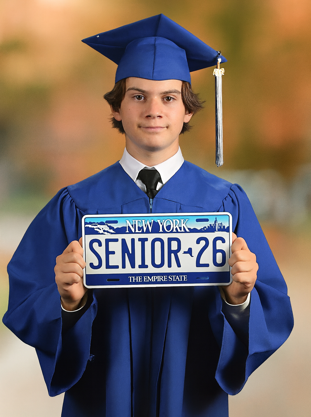 Ricardo Candelas in graduation cap and gown holding Senior 26 license plate